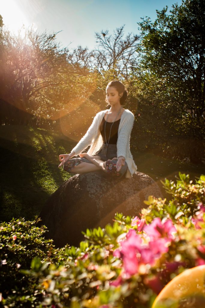 Woman meditating in a garden, seated on a rock