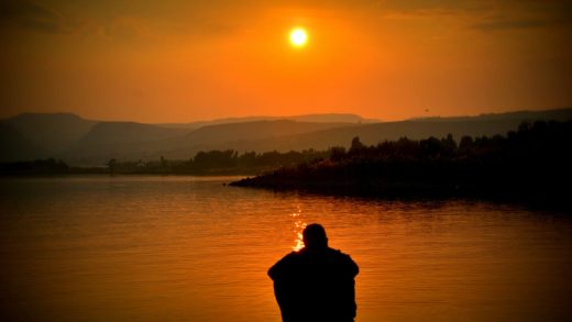 silhouette of person sitting beside body of water